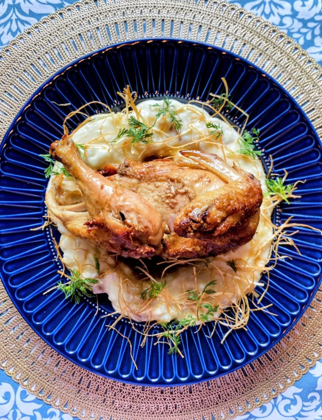 Codorniz dorada sobre puré, con papa paja y hierbas, en plato azul