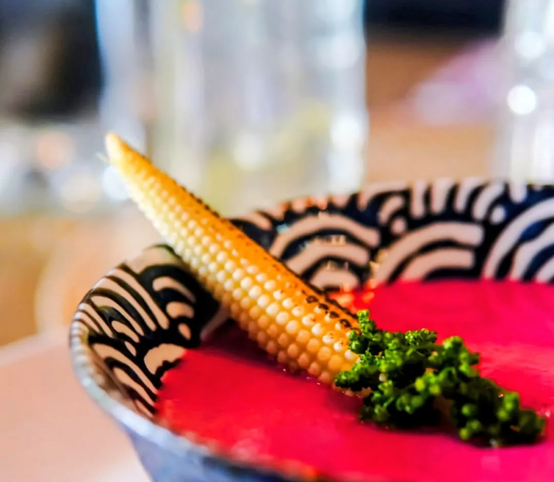 Elote baby asado sobre una crema rosa intenso, con un brote verde