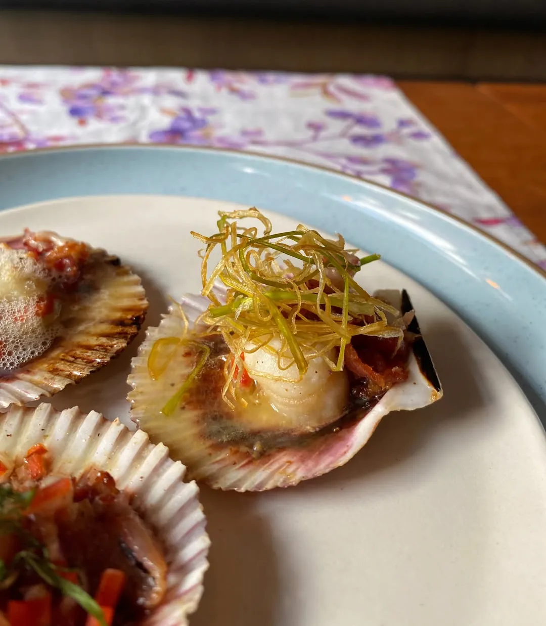 Zamburiña en su concha con poro frito, sobre plato claro
